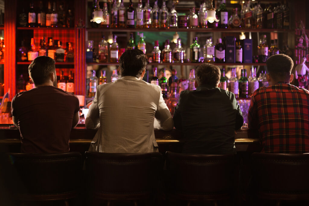Four men sitting at a bar at night.